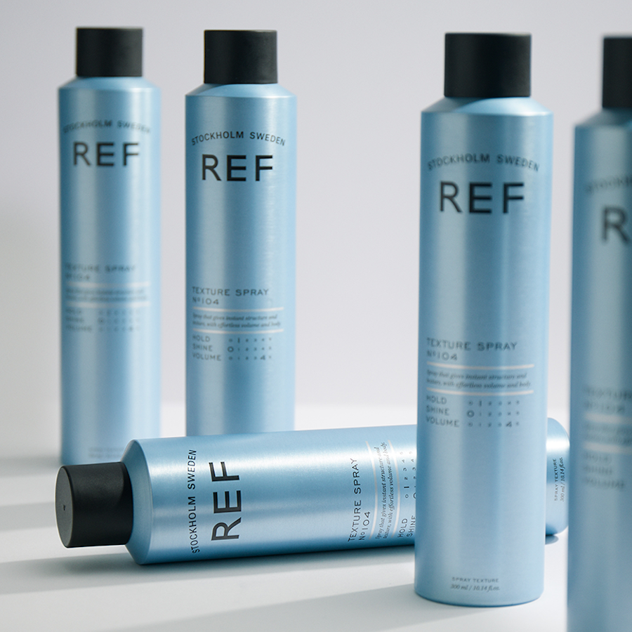 Genuine REF product photo (authorized distributor asset pack) — alternate angle group shot showing multiple Texture Spray N°104 cans, one lying on its side.